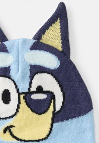Berretto lavorato a maglia in blu e navy con accenti gialli, caratterizzato da un grande viso di un personaggio dei cartoni animati e orecchie sollevate. Tessuto morbido e texturizzato.