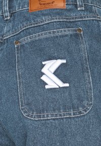 Mörkblå denimshorts med en vit broderad logotyp på bakfickan, synlig sömnad och en läderlogotyp vid midjan.