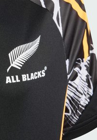Čierna športová košeľa s bielym logom paprade a textom "ALL BLACKS". Doplnkovaná oranžovými akcentami a vzorom po boku.
