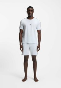 Vaaleansininen lyhythihainen t-paita, jossa on pyöreä kaula-aukko ja logo, yhdistettynä yhteensopiviin shortseihin. Kangas vaikuttaa sileältä ja mukavalta.