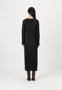 Μαύρο φόρεμα με μακριά μανίκια και κάθετες πτυχές, στρογγυλή λαιμόκοψη και ρέουσα σιλουέτα, συνδυασμένο με καφέ μποτάκια με τακούνι.