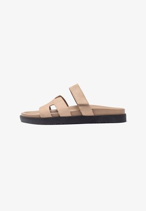 Sandales à glissière en suède beige avec une semelle en caoutchouc noir, dotées de deux larges sangles et d'un design découpé pour la ventilation et le confort.