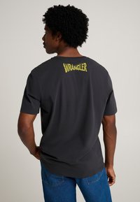 Tummanharmaa lyhythihainen puuvillainen t-paita, jossa keltainen "WRANGLER"-teksti brodeerattu niskan taakse. Yksinkertainen, rento malli.