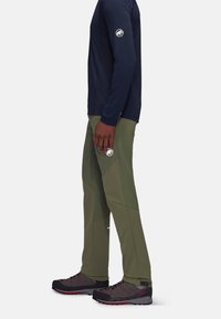 Marineblauw langemouwen shirt en olijfgroene technische broek, met een logopatch. Grijs en zwarte schoenen met rode accenten maken de outfit compleet.