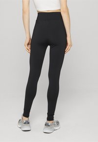 Svarte leggings med høyt liv, glatt tekstur, tettsittende design og uten synlige sømmer, kombinert med grå treningssko.