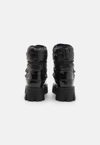 Black patent leather ankle boots with padded upper, lace-up detail, and chunky rubber sole. Features a textured finish and supportive design.