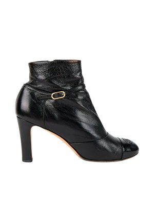 Bottine noire en cuir avec talon de hauteur moyenne, petite bride à boucle dorée et texture légèrement froissée sur la partie supérieure.