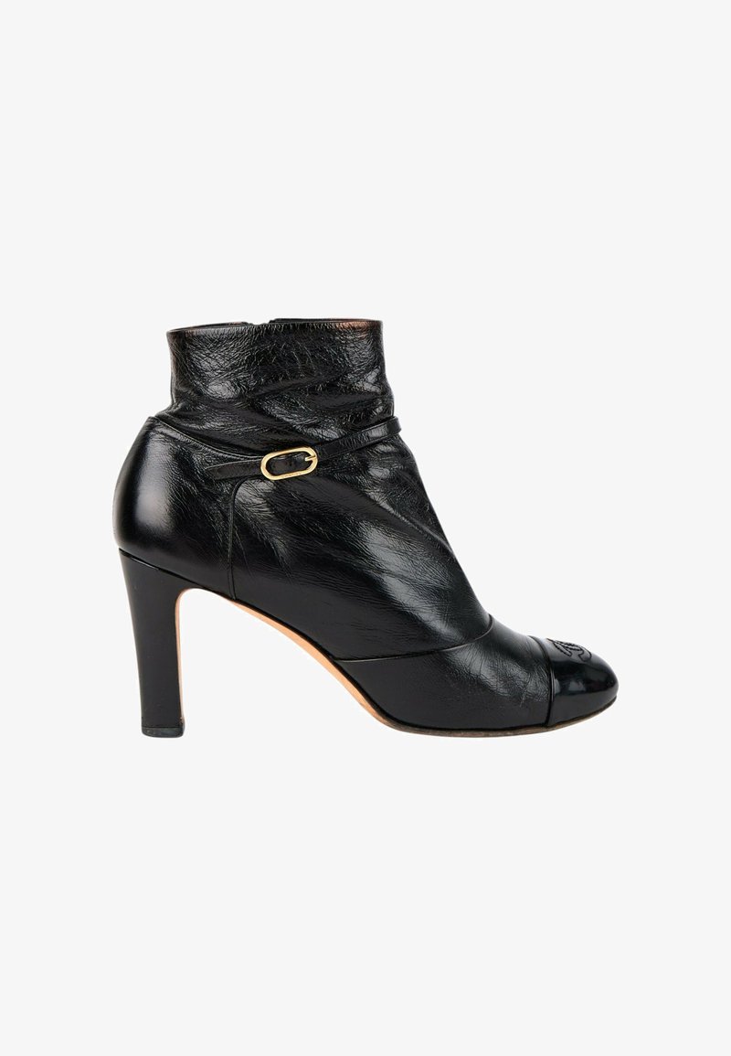 Bottine noire en cuir avec talon de hauteur moyenne, petite bride à boucle dorée et texture légèrement froissée sur la partie supérieure.