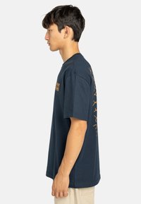 Marineblauwe katoenen t-shirt met korte mouwen. Heeft gouden tekst en graphics aan de voorkant en op de achterkant. Losse pasvorm.