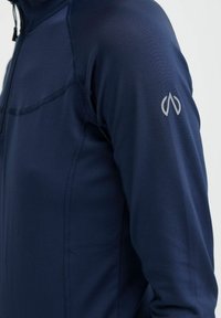 Tengerészeti sportos felső sima anyagból, fél cipzáros kialakítással, lapos varrásokkal és egy kis ezüst színű logóval a felső karon.