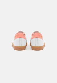 Bílé sneakers s oranžovými akcenty, strukturovaný kožený povrch, plochá gumová podrážka a minimalistický design. Zadní pohled ukazuje detail paty.
