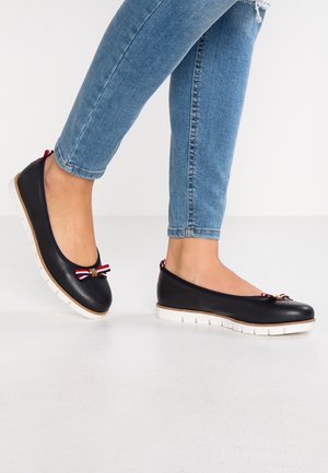 Black leather ballet flats feature a white sole, a red and blue bow accent on the toe, and a smooth texture.