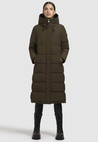 Lungo cappotto imbottito verde oliva con cappuccio, dotato di chiusura con zip, tasche laterali e un design trapuntato. Accenti neri e cerniere robuste.