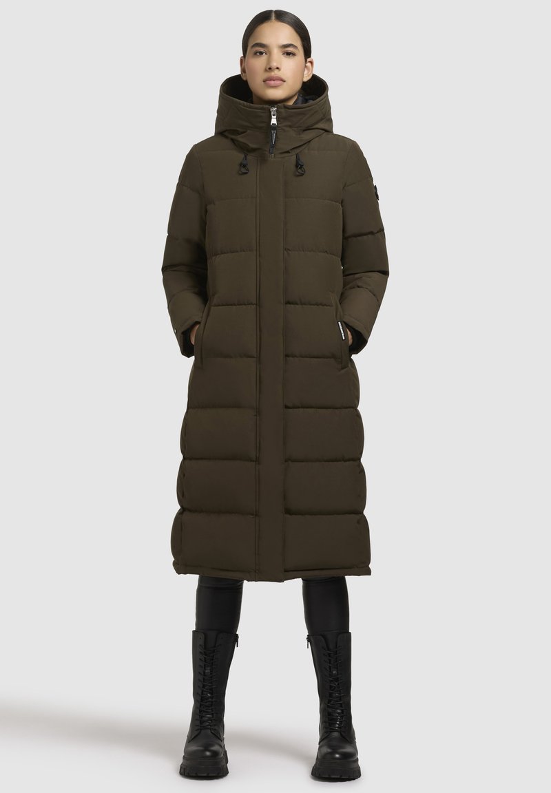 Lungo cappotto imbottito verde oliva con cappuccio, dotato di chiusura con zip, tasche laterali e un design trapuntato. Accenti neri e cerniere robuste.