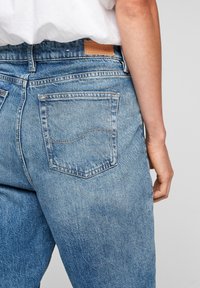 Light blue denim jeans with a relaxed fit, featuring two back pockets with subtle stitching detail and a tan leather patch at the waistband.