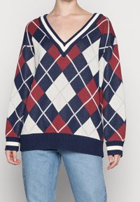 Pull à col en V avec un motif argyle en rouge, marine et blanc, doté de poignets et d'un ourlet côtelés, fabriqué en tissu tricoté texturé.