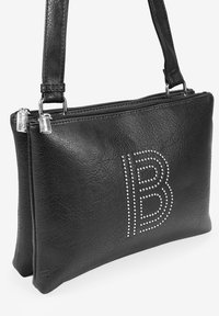 Bolso de mano de cuero negro con un acabado texturizado, que cuenta con dos compartimentos con cremallera y un diseño en forma de "B" de piedras brillantes plateadas en la parte delantera.