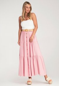Rosa gestufte Maxikleid mit durchgehender Knopfleiste, kombiniert mit einem weißen Tanktop und einem beigefarbenen Woven-Gürtel. Getragen mit klobigen Sandalen.