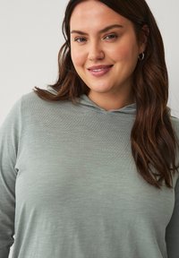 Maglione grigio chiaro con cappuccio e maniche lunghe, realizzato in un tessuto morbido e testurizzato. Presenta una vestibilità comoda e una leggera lucentezza sul materiale.