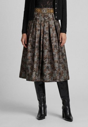 Jupe midi plissée fleurie avec un éclat métallique, associée à des bottes noires à talons montant jusqu’au mollet et un cardigan noir boutonné.