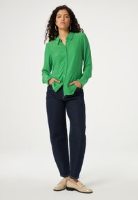 Groene zijden button-up shirt met lange mouwen, voorzakken, gecombineerd met donkerblauwe rechte jeans en beige loafers.