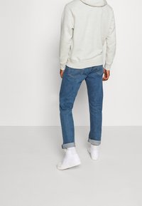 Grå huvtröja med huva, blå jeans i denim och vita högklackade sneakers. Jeans är uppvikta vid mudden och huvtröjan har en standardpassform.