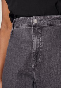 Šedé džínové kalhoty s vysokým pasem a hladkou texturou, s předním zapínáním na knoflíky, bočními kapsami a jemným akcentem značky.