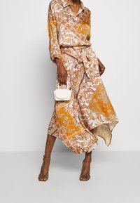 Robe longue à motifs orange et blanc avec des dessins cachemire ; dotée d'un col, de liens à la taille et d'un ourlet asymétrique. Petit sac blanc.