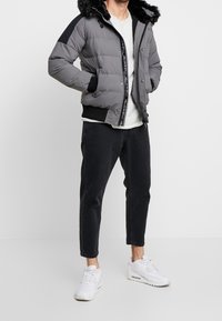 Grå puffjacka med svarta detaljer och krage av konstpäls, med zip-stängning och ribbade ärmmuddar, bärs över en ljus skjorta och mörka jeans.