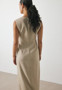 Beige ærmeløs kjole med et tætsiddende design. Stoffet ser glat ud med en subtil tekstur, med en bagsøm og en lang silhuet.