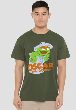 Olivegrünes Baumwoll-T-Shirt mit einem Grafik von Oscar dem Nörgler in einem Müllcontainer, mit fettem orangefarbenem Text "OSCAR DER NÖRGLER."