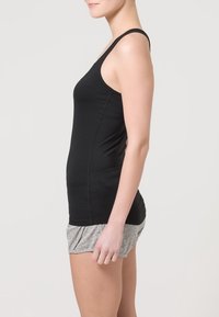 Černý přiléhavý top na ramínka s tenkými popruhy a hladkým materiálem, doplněný o šedé volné šortky s nařaseným pasem.