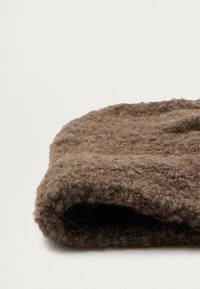 Bonnet tricoté marron en laine texturée avec une apparence douce et duveteuse. Le bord roulé présente un fil épais et des variations de couleur naturelles.