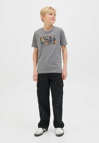 Šedé bavlněné tričko s multibarevným grafikou "JACK & JONES", spárované s černými cargo kalhotami a bílými teniskami se šedými akcenty.