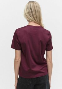 Burgundy t-paita lyhyillä hihoilla, pyöreällä kaula-aukolla ja löysällä mitoituksella. Sujuva puuvillakangas, ilman näkyviä kuvioita tai metalliosia.