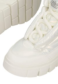 Masywne białe sneakersy z grubą fakturowaną podeszwą, wyściełanym wierzchem i grubymi plecionymi sznurowadłami, ukazujące szczegóły z przodu i z boku.