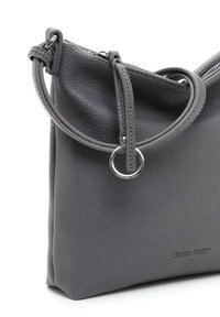 Borsa a spalla in pelle grigia con texture, dal design elegante, con manico curvo e un accento metallico circolare, etichettata "SURI FREY."