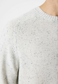 Hellgrauer Strickpullover mit einem strukturierten Muster, das blaue und dunklere Farbtöne enthält. Sichtbarer gerippter Halsausschnitt und Schulterschmuck.