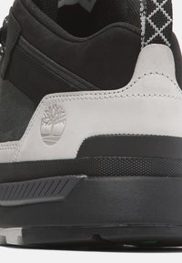 Svart och grå sneaker med ovandel i mocka och läder, strukturerade detaljer, gummisulor och en präglad logotyp på hälen.