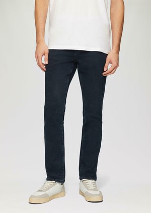 Donkerblauwe, slim-fit jeans van denim, met een klassieke vijf-pocket stijl en subtiele stiksels, gecombineerd met lichtgekleurde sneakers.