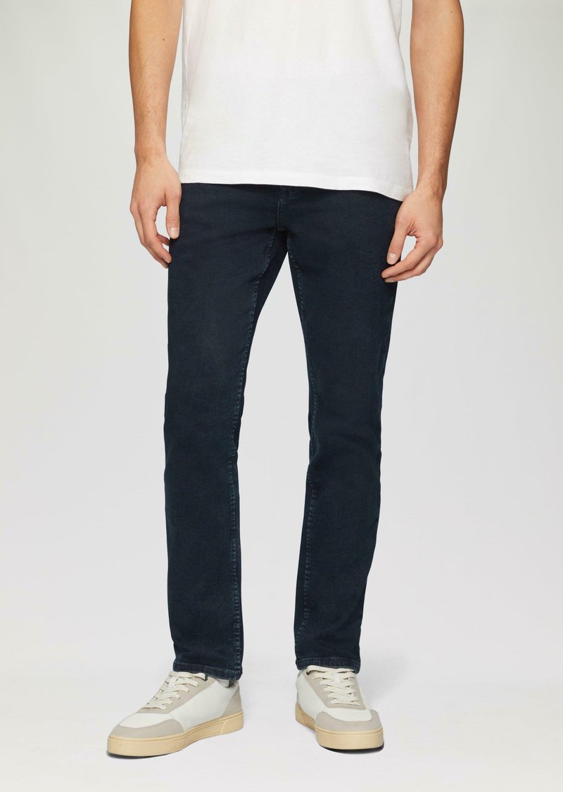 Dunkelblaue, slim-fit Jeans aus Denim mit klassischem Fünf-Taschen-Design und feinen Nähdetails, kombiniert mit hellen Sneakers.
