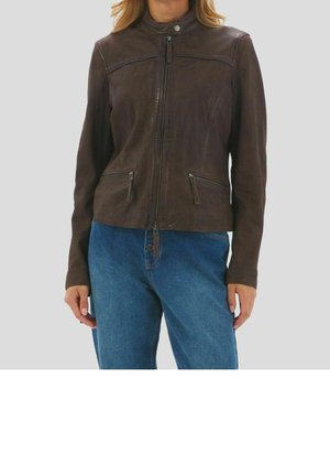 Vrouw draagt een donkerbruine leren jas met ritssluiting, twee ritszakken aan de voorkant en een hoge kraag, gecombineerd met een blauwe spijkerbroek.