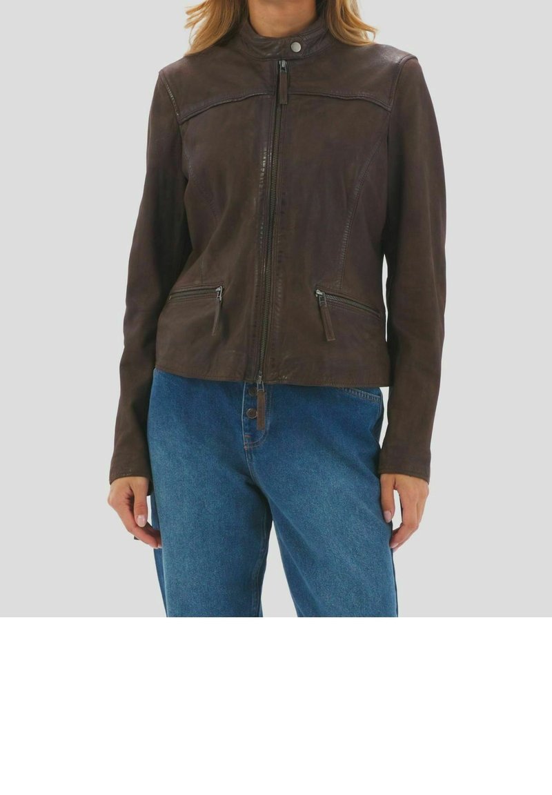 Femme portant une veste en cuir marron foncé à fermeture éclair, avec deux poches zippées à l'avant et un col montant, associée à un jean en denim bleu.