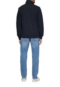 Sweatshirt bleu marine avec col montant, fabriqué en tissu doux. Assorti à un jean bleu clair. Des chaussures blanches complètent la tenue.