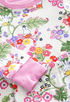 Vêtement en coton à motif floral avec des poignets roses. Présente des lapins dessinés parmi des fleurs éclatantes dans des nuances de rose, vert et violet.