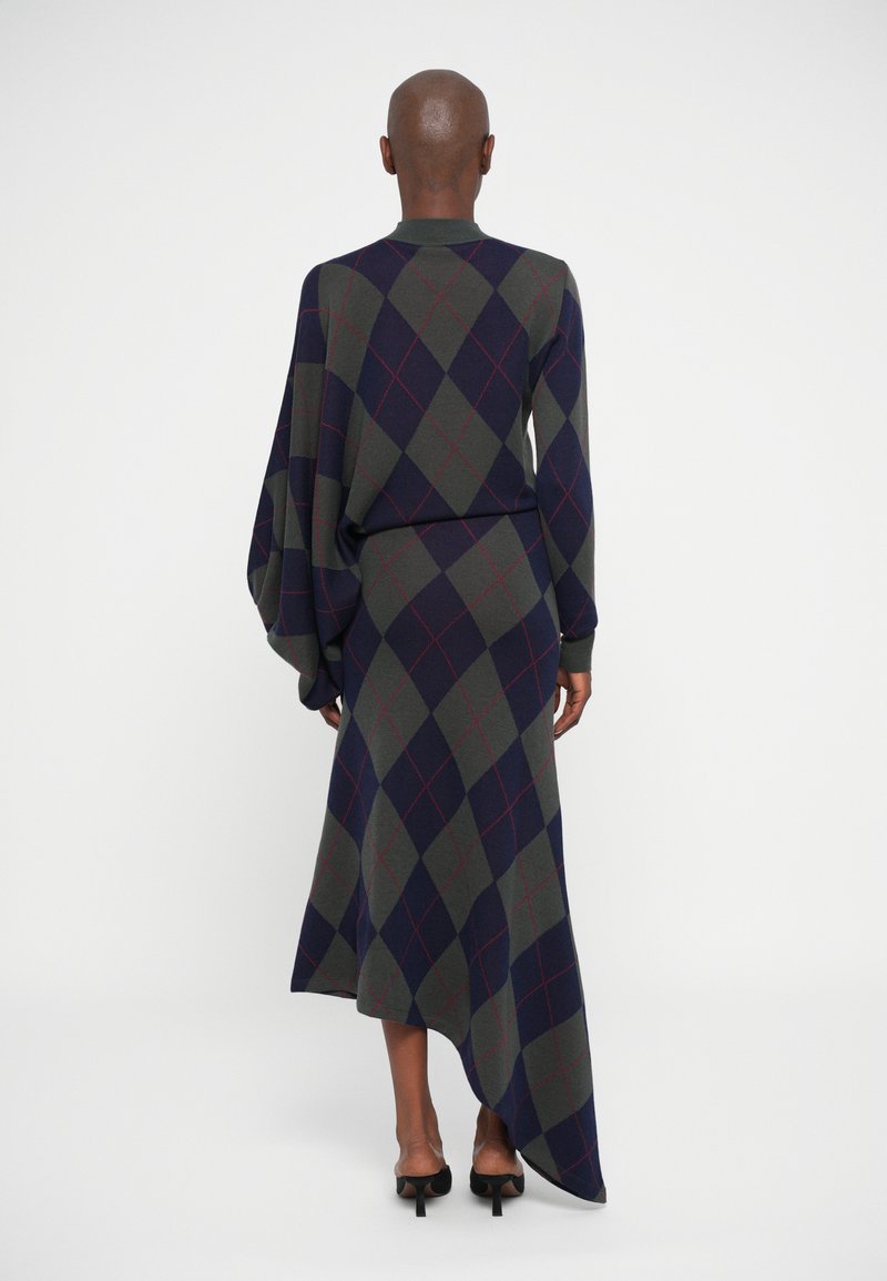 Langarm, asymmetrische jurk met een donkerblauw, groen en rood ruitpatroon, gemaakt van een gestructureerd breimateriaal.