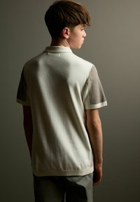 Lysefarvet polo shirt med korte ærmer, strukturerede grå strikdetaljer på skulderne og en klassisk krave. Glat stof med en tætsiddende pasform.
