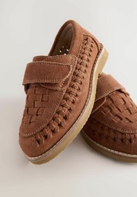 Braune Wildlederschuhe mit einem gewebten Design, Klettverschluss und Gummisohle. Texturierte Oberfläche mit einer flachen, abgerundeten Zehenpartie.