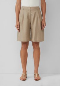 Shorts plissés beiges en matériau léger, longueur genou, avec une texture lisse et une coupe ajustée. Associés à des sandales dorées.