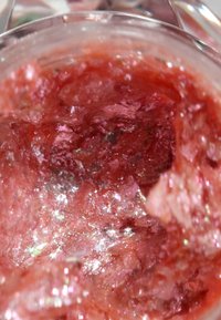 Roter Schimmerpeeling in einem klaren Glasbehälter, mit einer glänzenden, kristallinen Textur und pinken sowie silbernen Funkeln, die im Licht erstrahlen.
